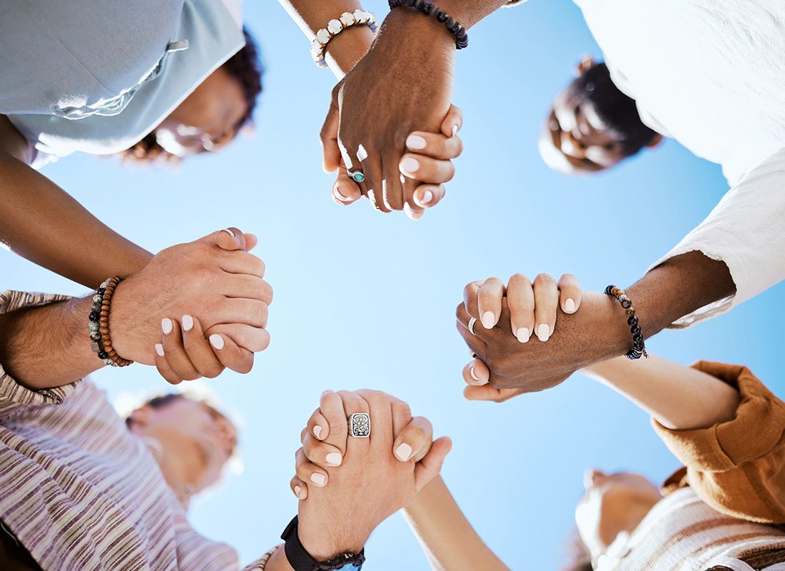 Community Involvement - View Looking Up at Four Individuals Standing Around a Circle While Holding Their Hands Together in Unity Against a Blue Sky
